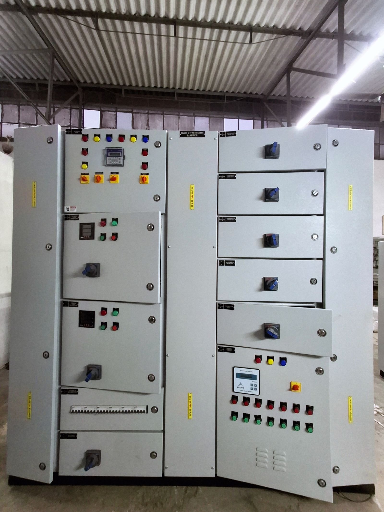 Front elevation of a floor-standing LT panel in three vertical sections: a control section with pushbuttons and a digital relay, a central busbar chamber, and a right-hand section of switch-disconnector compartments above a power factor correction section with staged indication.