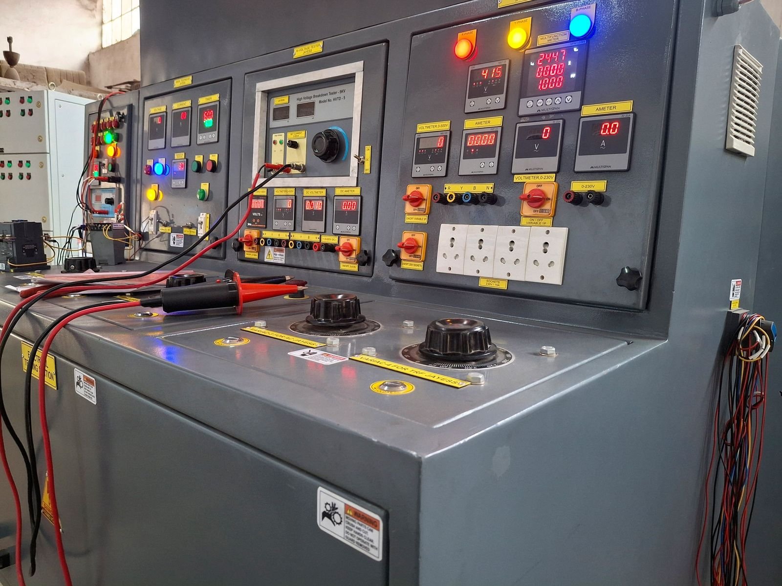 The testing console seen from the side, showing the instrument panels in perspective with the variac knobs along the working surface and test leads connected.